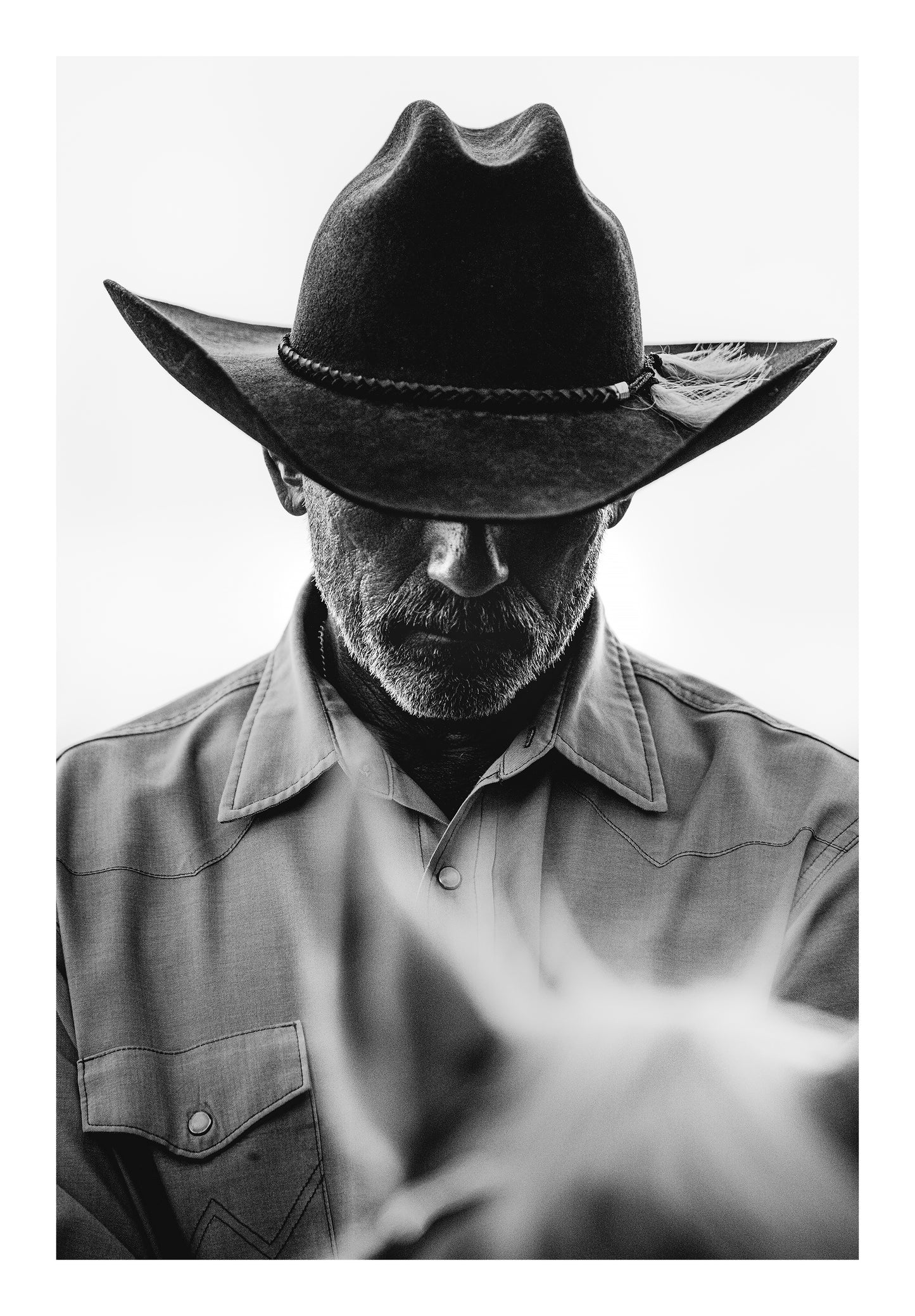 Minimalist black and white fine art photograph of a cowboy in a cowboy hat on a horse with a rugged western look. 