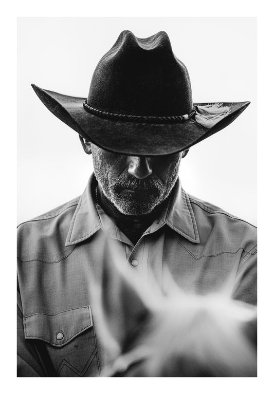 Minimalist black and white fine art photograph of a cowboy in a cowboy hat on a horse with a rugged western look. 