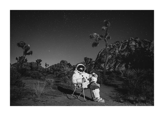 An astronaut sitting in a midcentury lawn chair in Joshua Tree National Park. 