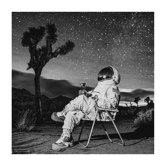 Astronaut sitting in a midcentury lawn chair under a starry night sky while drinking a martini. 