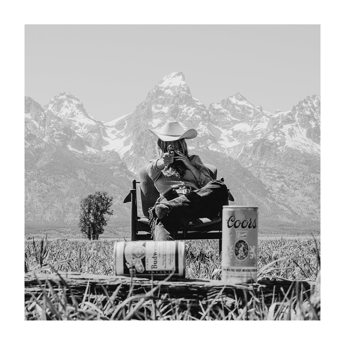 Black and white photography of a western cowgirl aiming a gun at old beer cans in front of the Grand Tetons in Jackson, Wyoming. 